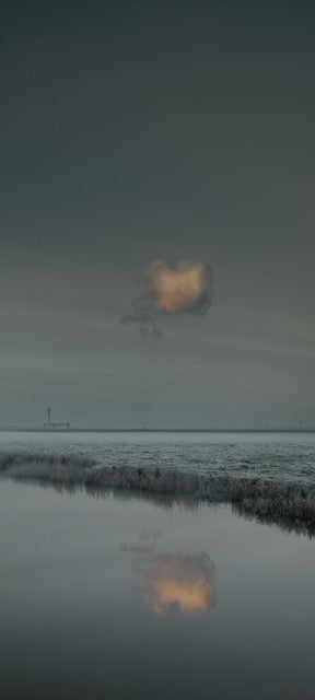 Colour photo of water and a sky with one yellow cloud. The horizon is just below the middle and in the water you see the reflection of the one cloud.