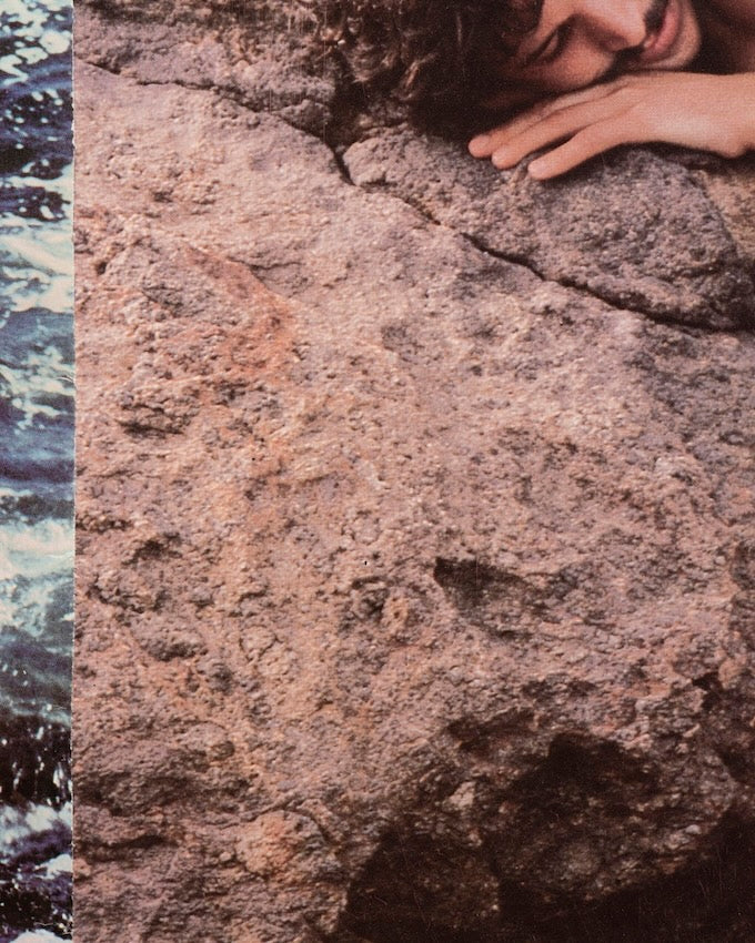 kleurenfoto van man met hoofd op rots en links een strook zee