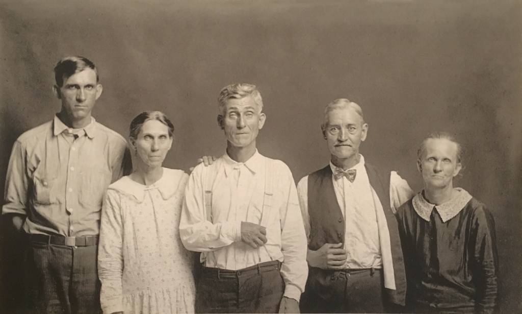 horizontal black and white image of a group of 5 people in front of a dark backdrop