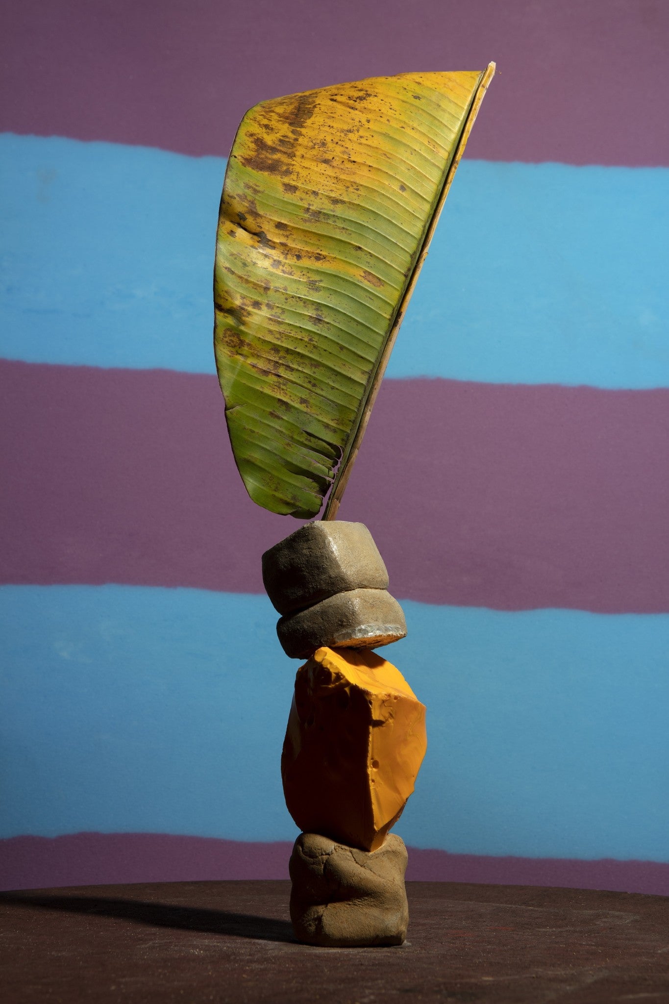 Clay, stones and a leave stacked on top of each other in front of a purple and blue striped background