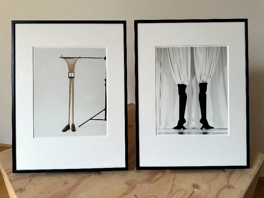set of two framed first editions in a black aluminium frame with matting, standing next to each other on a wooden block