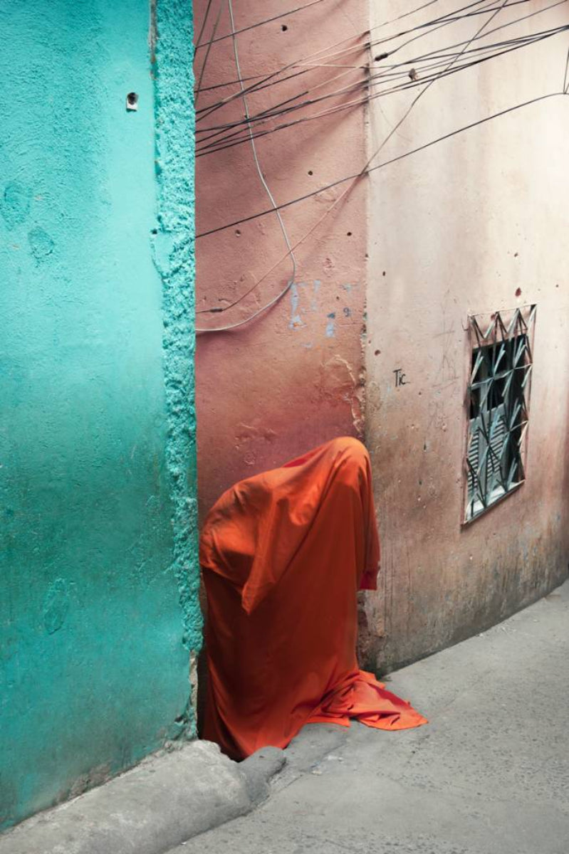A figure covered in orange fabric in between a pink and blue building