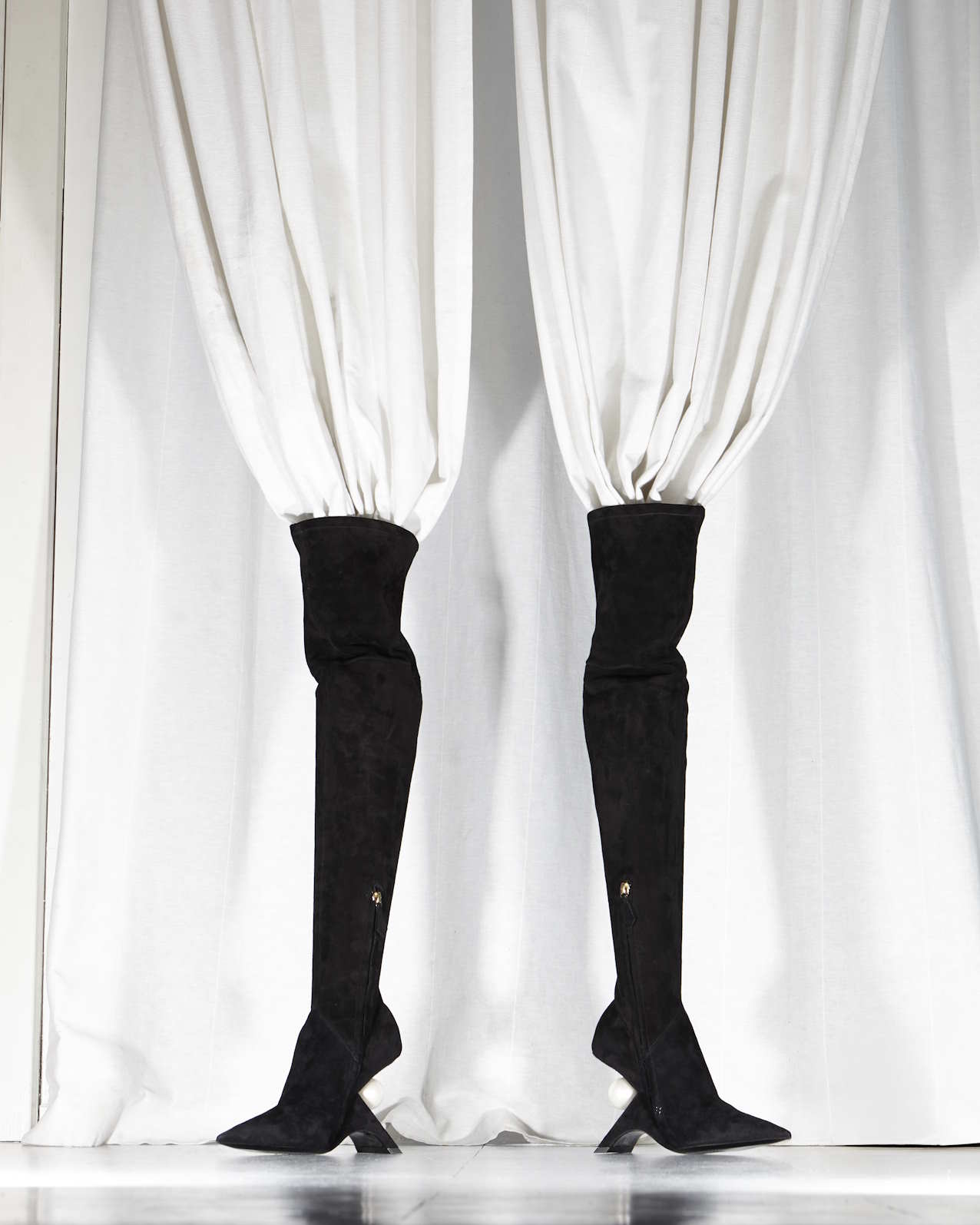 two high black boots standing up with white curtains in them, blending in the background
