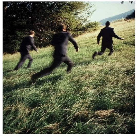 Three men in black suits running on a green hill