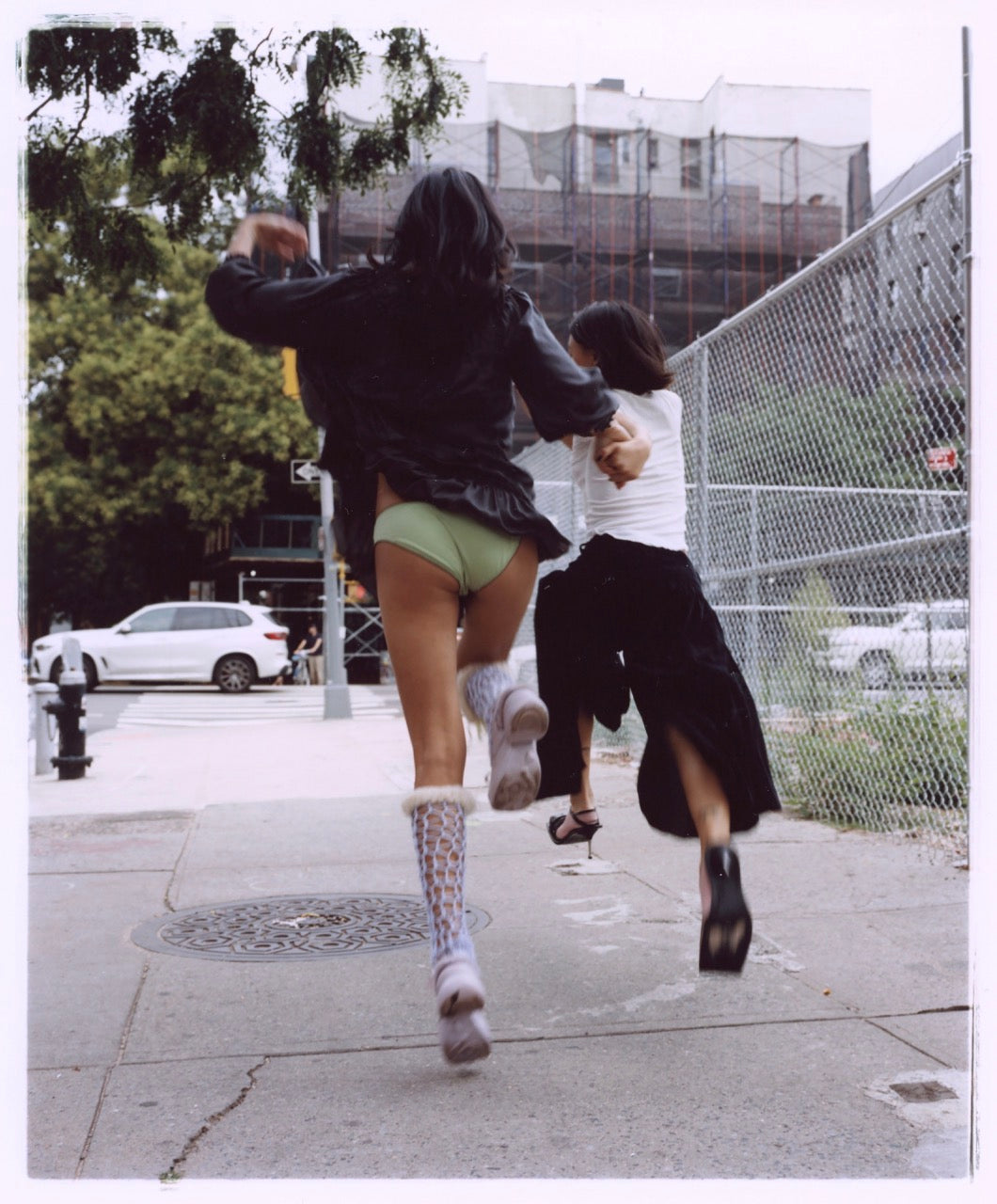 Colour photo of two young women on a city street, holding hands while skipping 