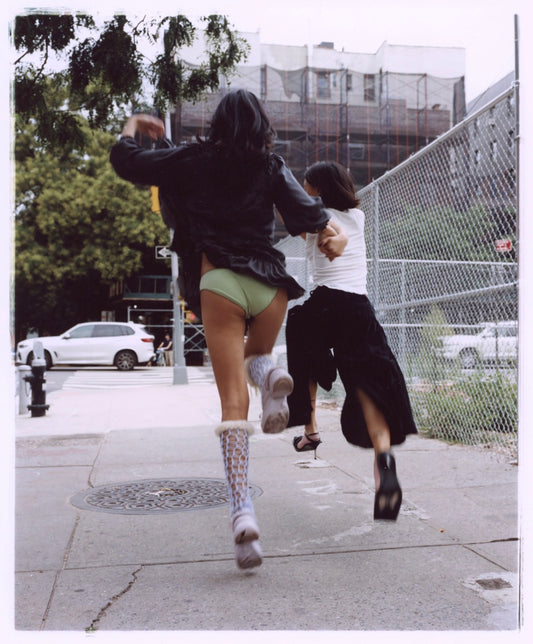 Colour photo of two young women on a city street, holding hands while skipping 