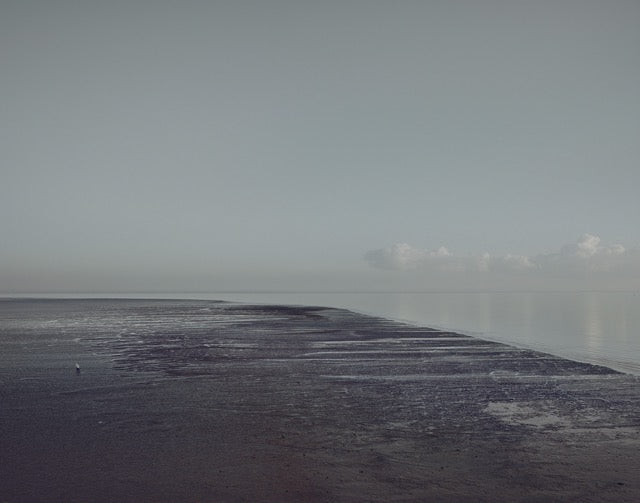 Colour photo of sea shore line on the left and a horizon in the middle of the photo. On the right a small group of white clouds. 