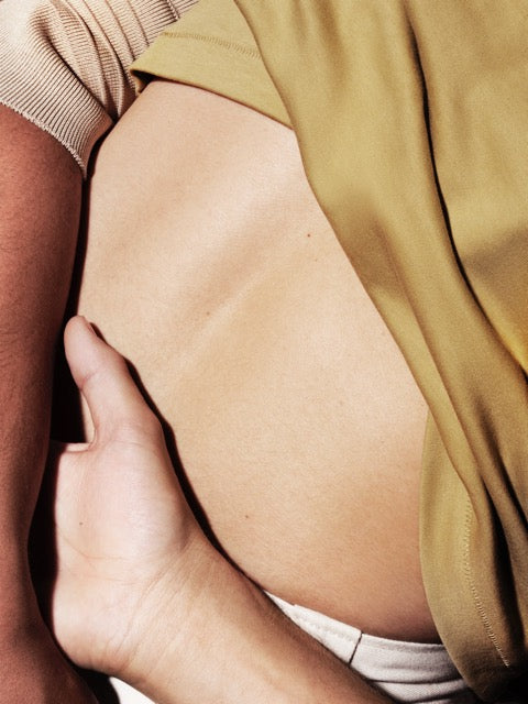 Colour photo of a back with yellow shirt, showing skin, an arm and a hand