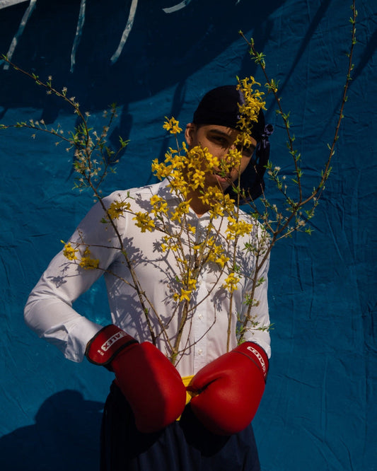 Figure in white shirt, wearing red boxing gloves holding yellow flowers in front of blue background