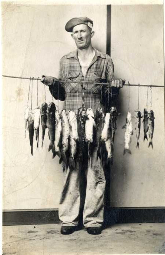 black and white photo of a person holding a stick with hanging fishes attached to it 