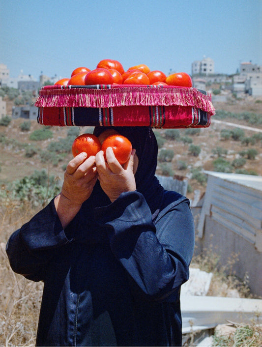 A women holding two oranges in front of her face, carrying a basket of oranges on her head