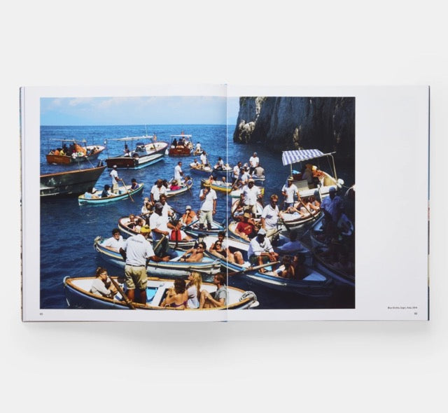 Spread showing one colour photo of a bay between high rocks filled with small boats, filled with people.