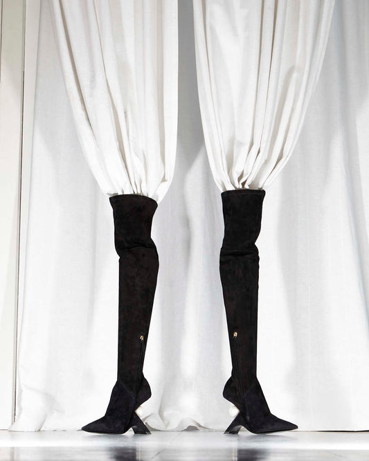 two high black boots standing up with white curtains in them, blending in the background